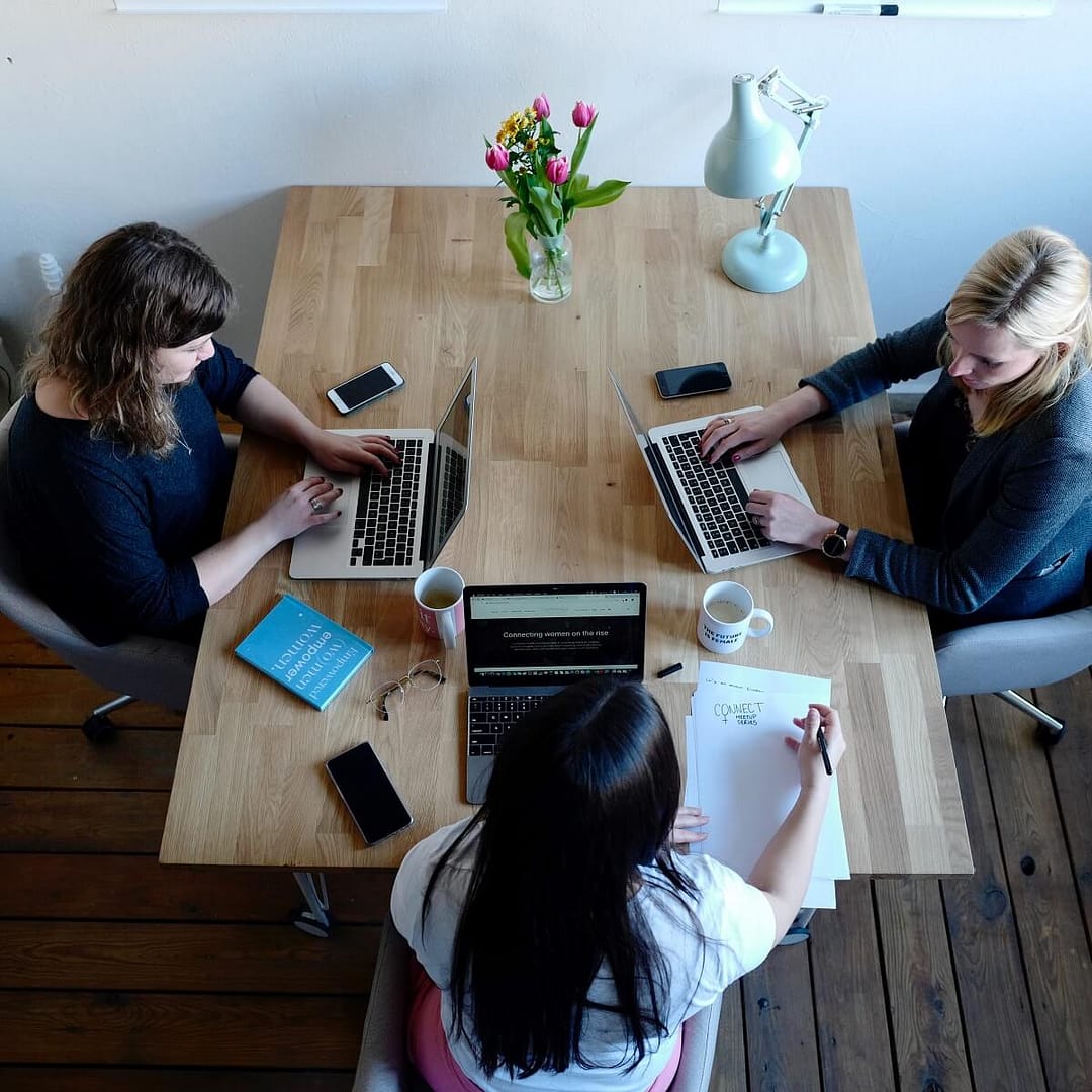 Three women are sitting around a table with laptop and having a meeting.